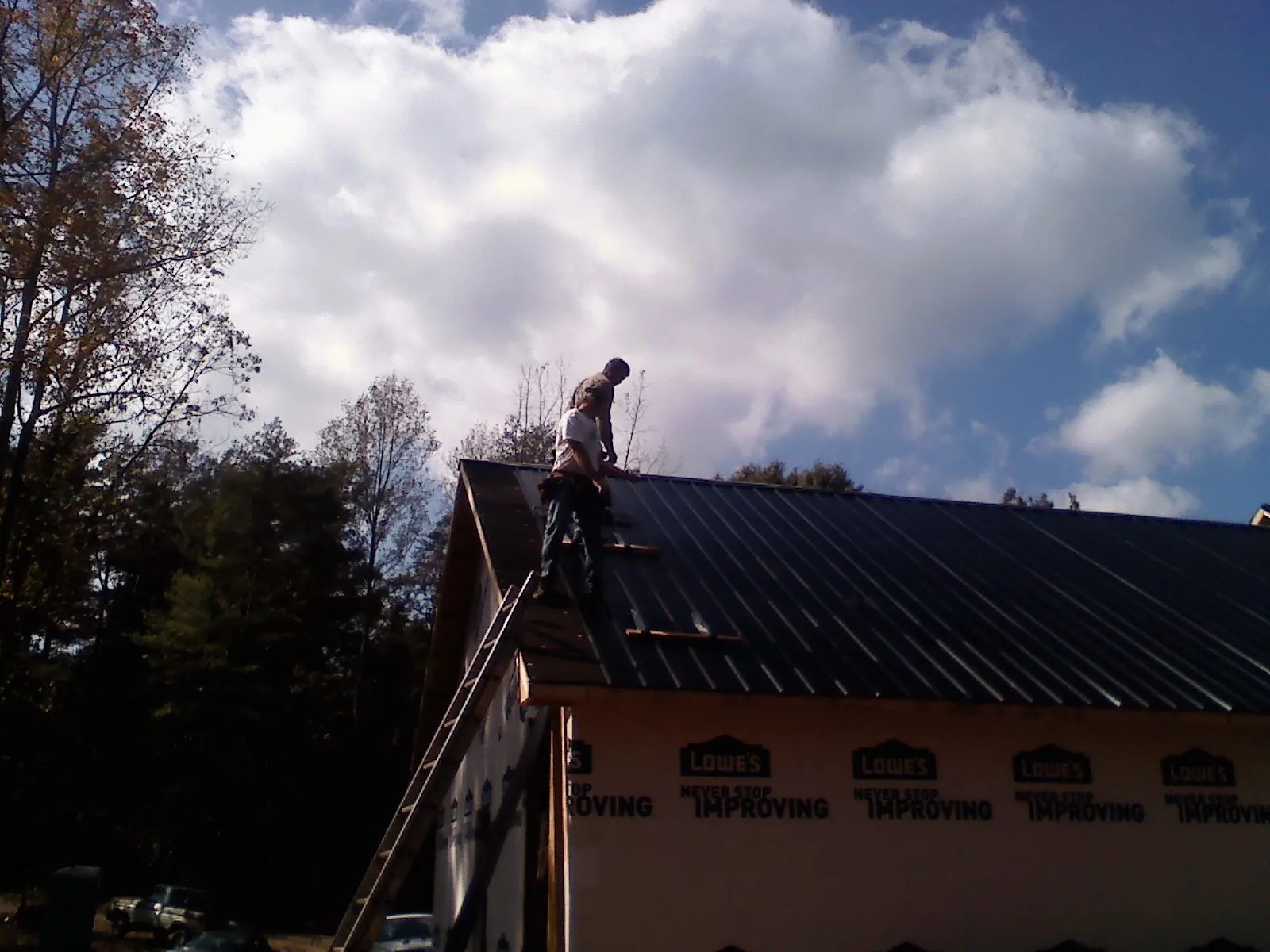 Roofer fastening dark metal panels high against a cloudy sky, from a Roof Inspection job in Lovejoy