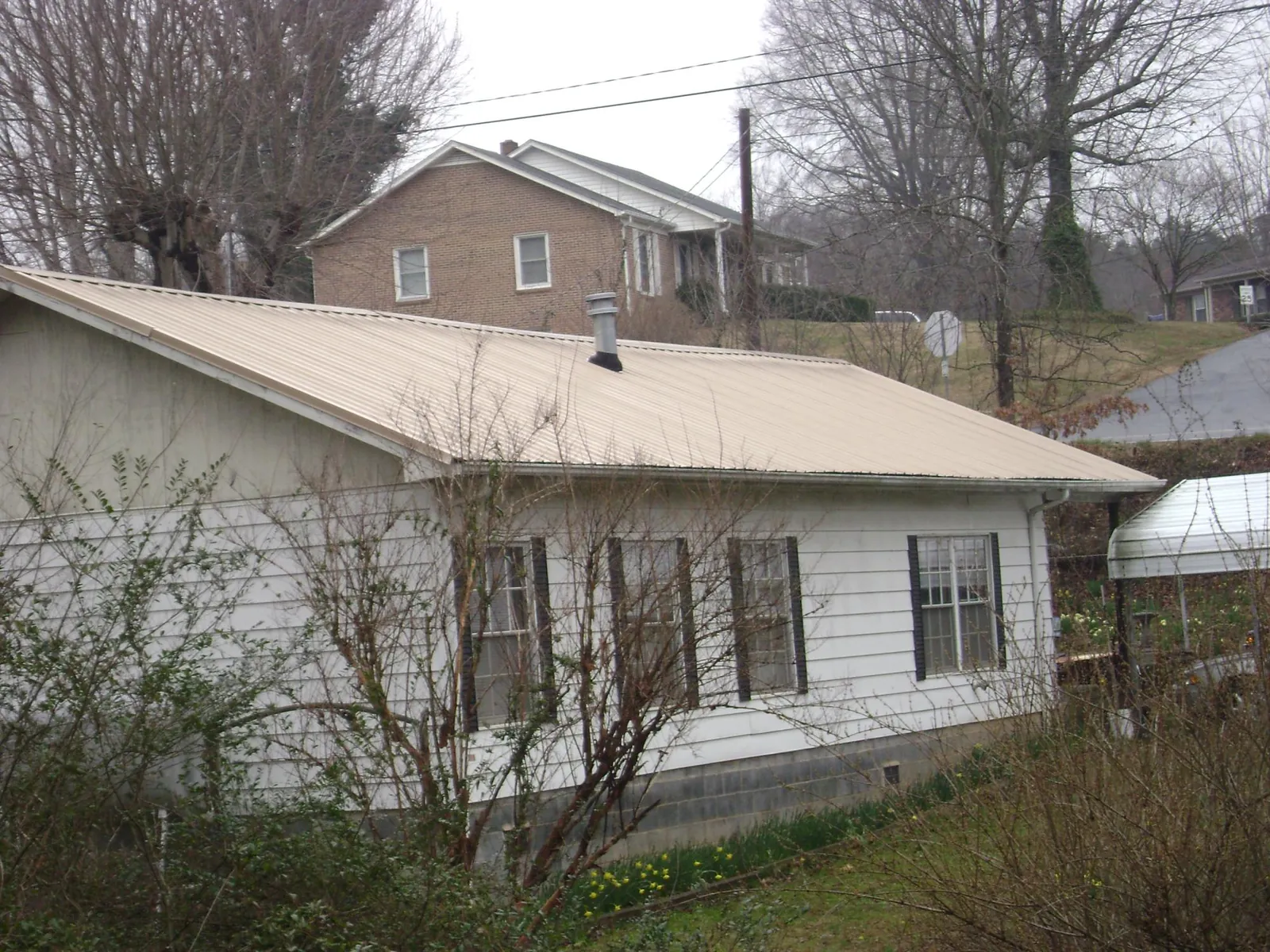Tan metal roof on a white sided house set into a hillside — Commercial Roofing by Roofing Brothers in Lovejoy
